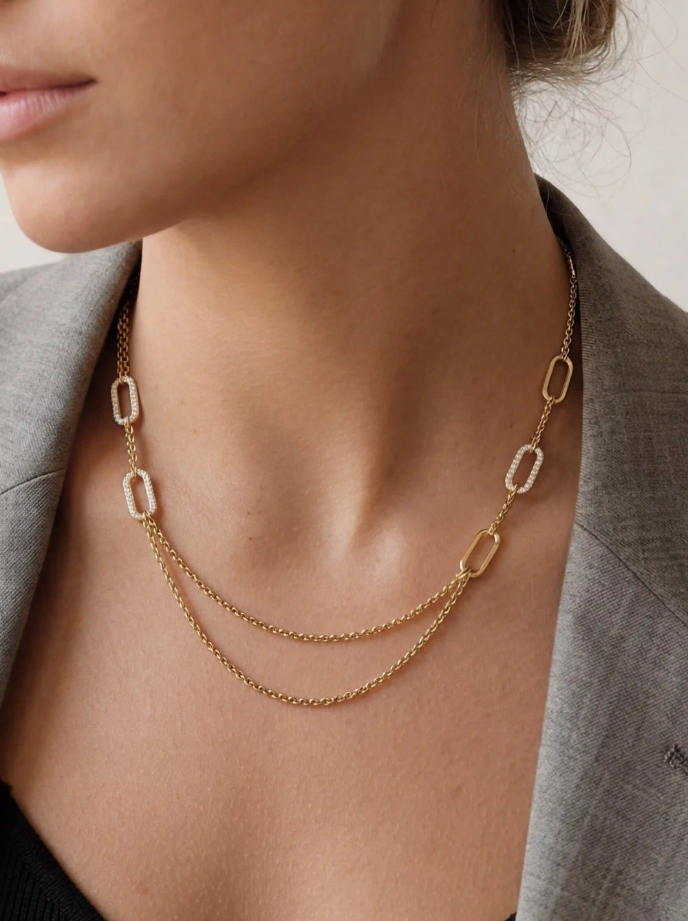 Close up of woman wearing gold Daphne draped necklace with pave crystal links and grey blazer office chic.