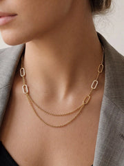 Close up of woman wearing gold Daphne draped necklace with pave crystal links and grey blazer office chic.