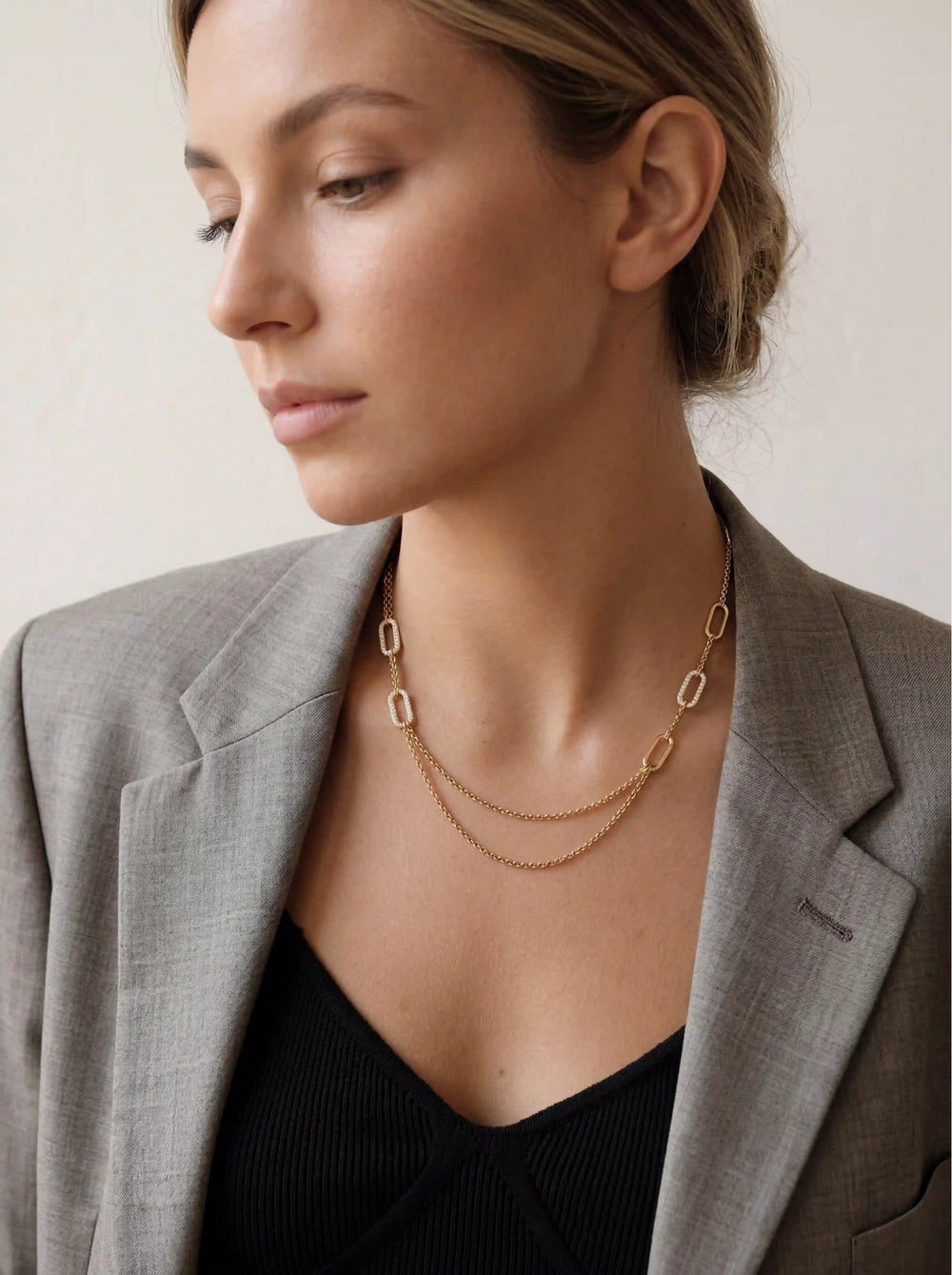 Lifestyle photography of woman styling pre-layered gold chain necklace with grey suit professional look.