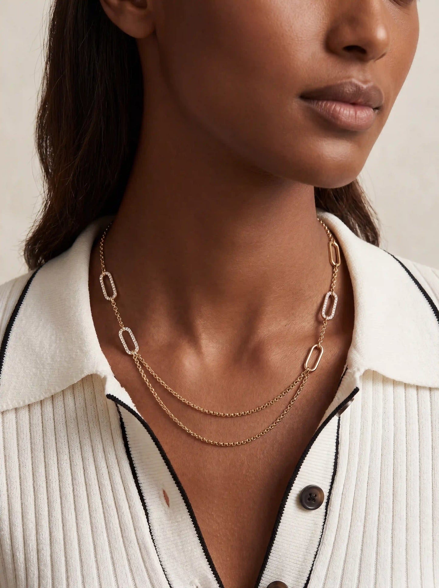 Model with dark skin wearing gold layered chain necklace with white ribbed shirt modern aesthetic.