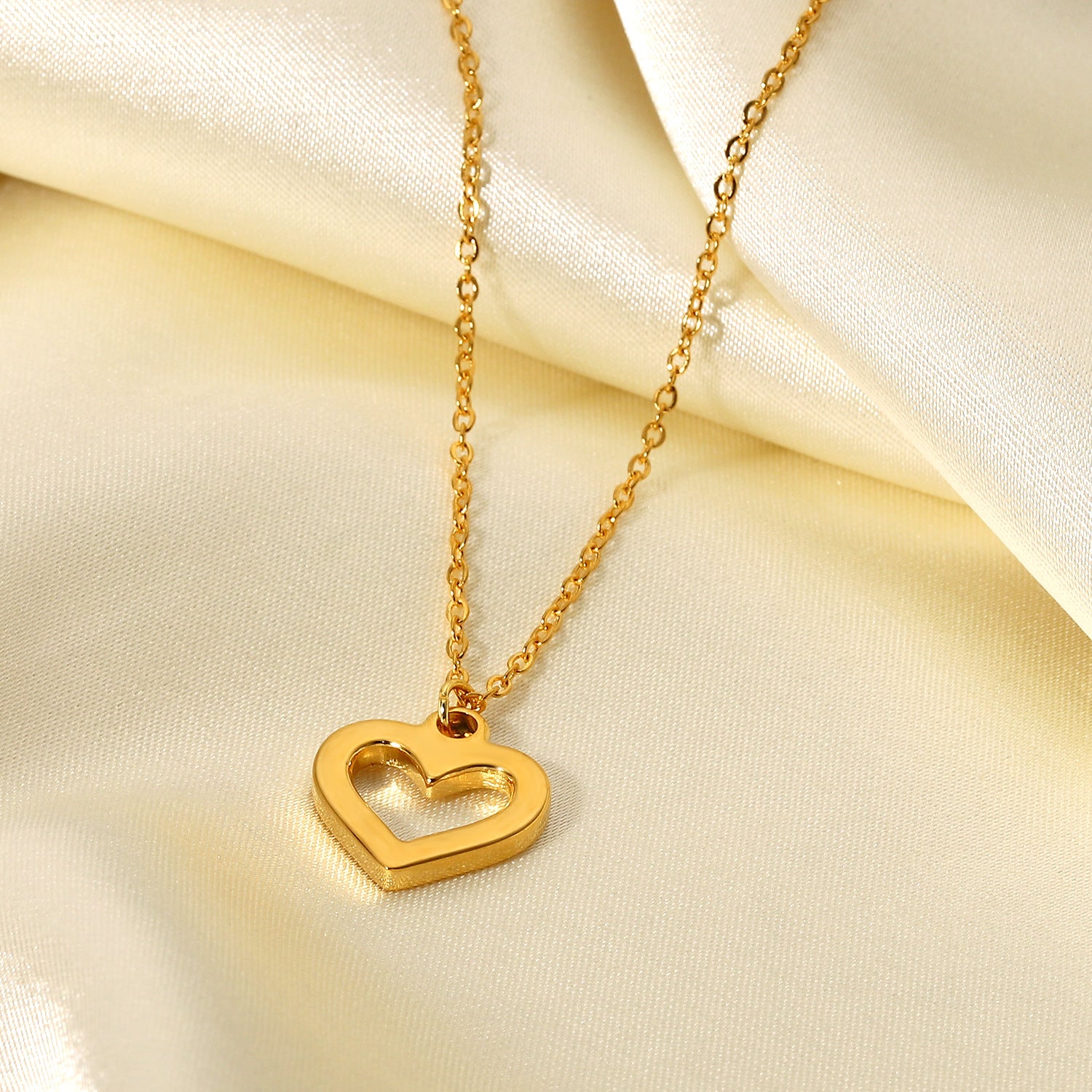 The Devotion Necklace displayed on a luxurious, flowing silk background, showing the full length of the delicate gold chain and the shimmering heart pendant.