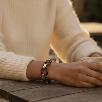 A detailed close-up of the Florence Link Bracelet on a woman's wrist, resting on a wooden table in the warm sunlight, highlighting its rich colors and textures.