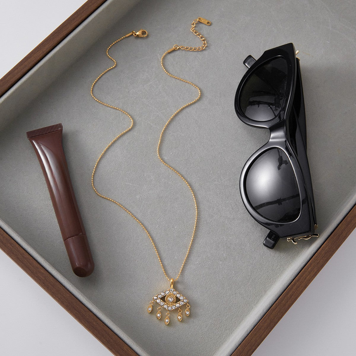 The Fortuna Necklace styled as an everyday essential in a leather tray, alongside sunglasses and lipstick, perfect for the modern woman.