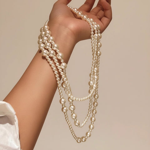 A model's hand holding the luxurious cascade of The Gabrielle Necklace, showcasing its opulent length and lustrous pearls.