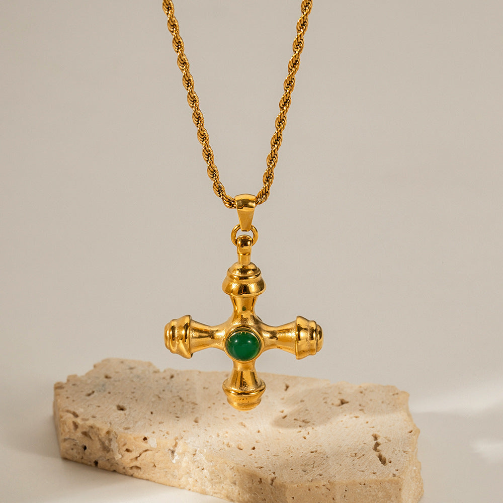 The Jupiter Necklace featuring the vibrant Green Agate cross pendant, resting on a stone to showcase its rich color and heirloom quality.