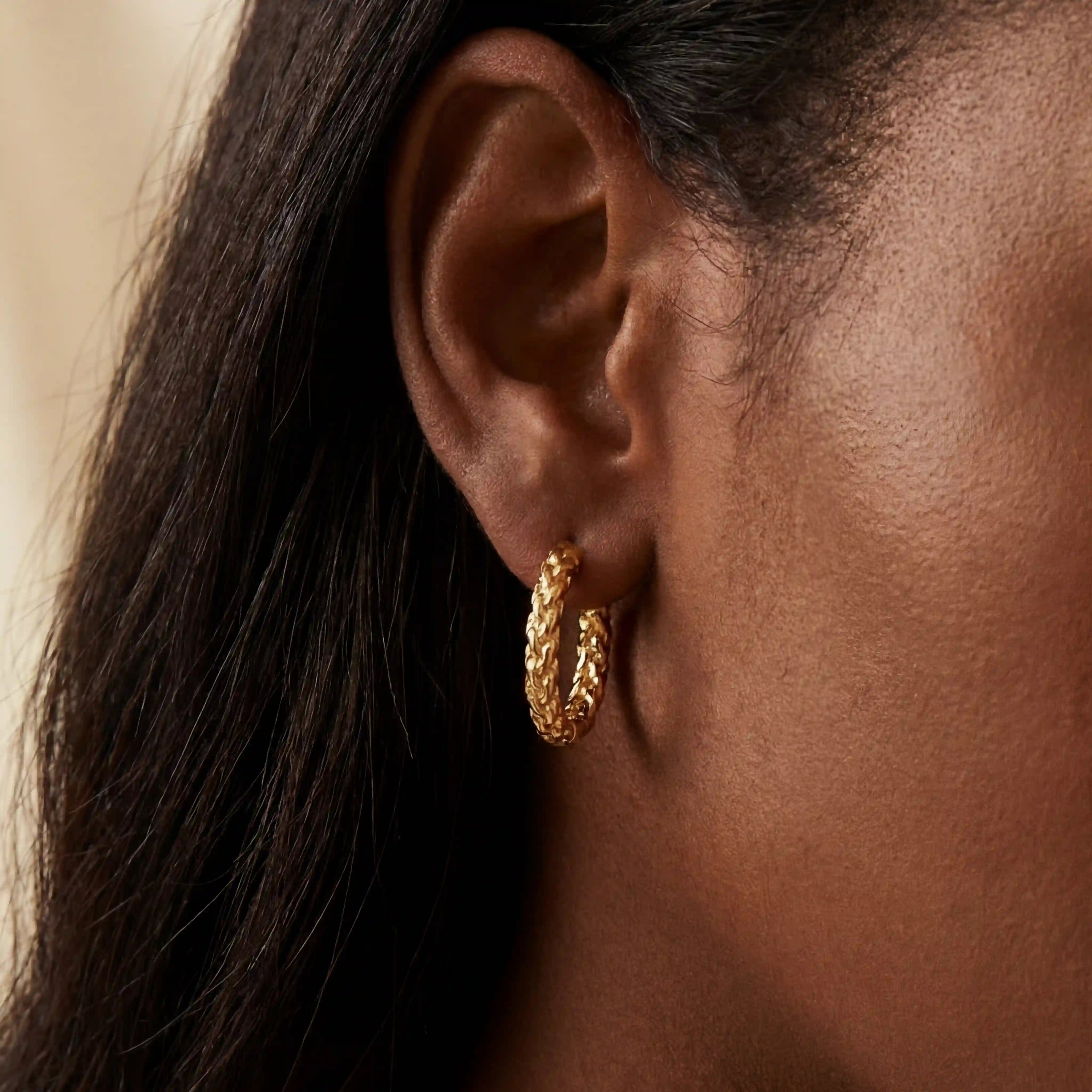 Gold crushed texture hoop earrings on dark skin, sparkly diamond-cut finish hoops, hypoallergenic stainless steel jewelry for sensitive ears. Main image
