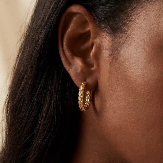 Gold crushed texture hoop earrings on dark skin, sparkly diamond-cut finish hoops, hypoallergenic stainless steel jewelry for sensitive ears.