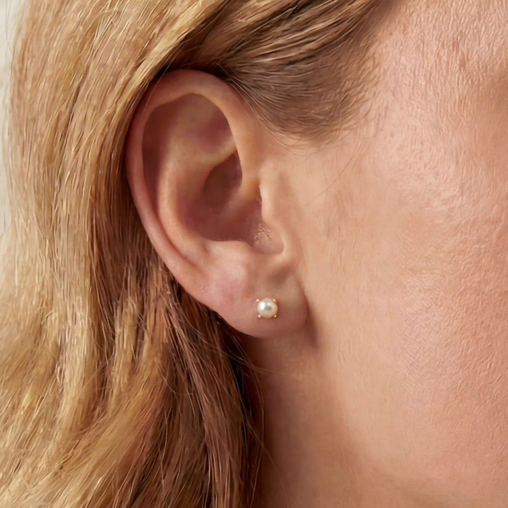 Tiny pearl stud earrings on ear lobe, minimalist second hole earrings, hypoallergenic stainless steel jewelry for sensitive skin.