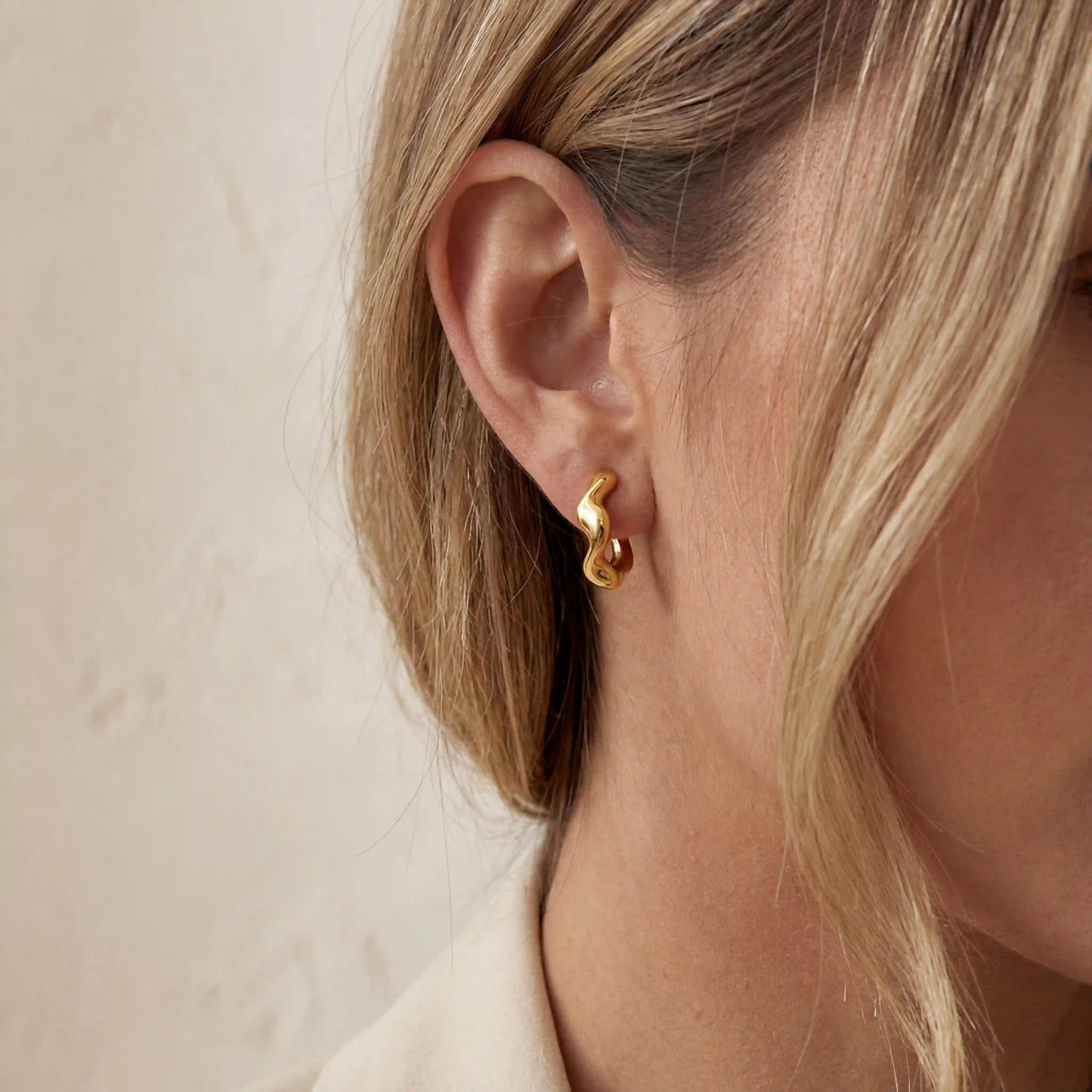 Close up of Nola organic wave gold hoops, small melted gold style earrings on ear, hypoallergenic stainless steel jewelry for sensitive ears.