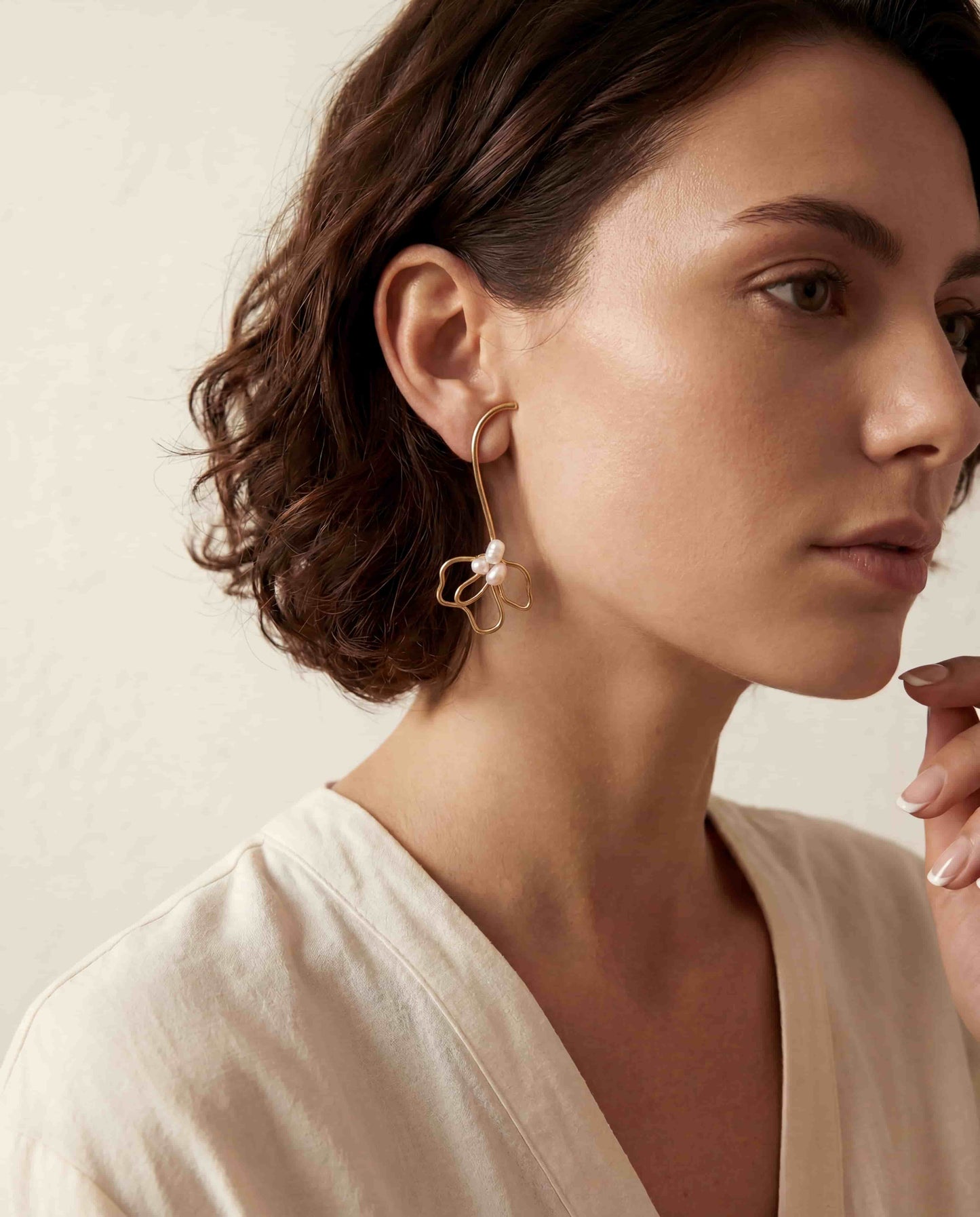 Brunette model wearing gold pearl floral drop earrings with white button down shirt office chic.