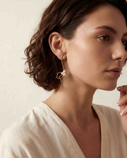 Brunette model wearing gold pearl floral drop earrings with white button down shirt office chic.