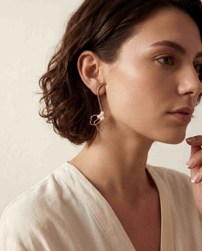 Brunette model wearing gold pearl floral drop earrings with white button down shirt office chic.