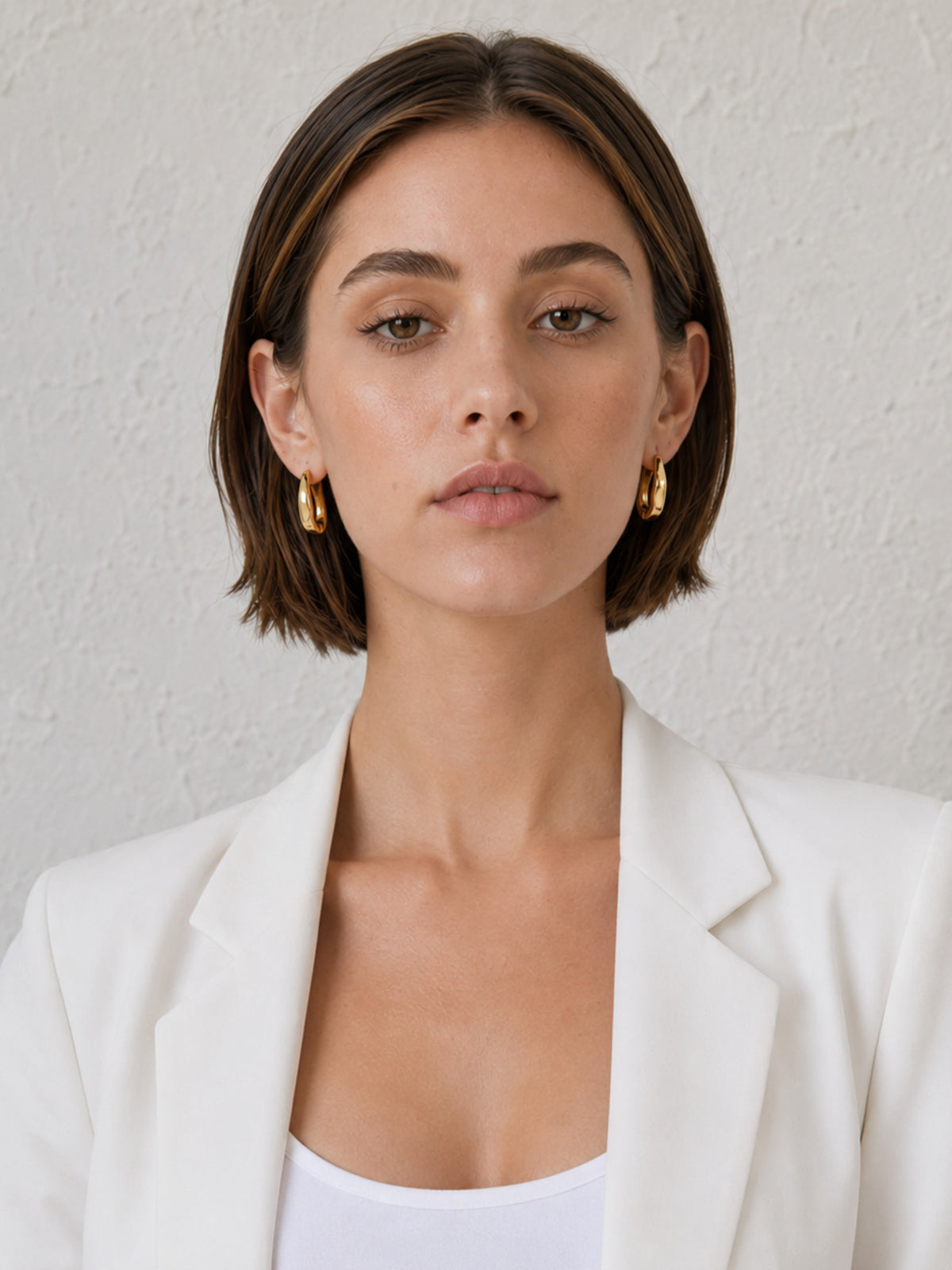 Model close-up wearing compact chunky gold huggie hoop earrings