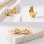 Aesthetic flat lay of textured gold hoops on stone prop, high-quality waterproof jewelry display, trendy gifts for her 2026.