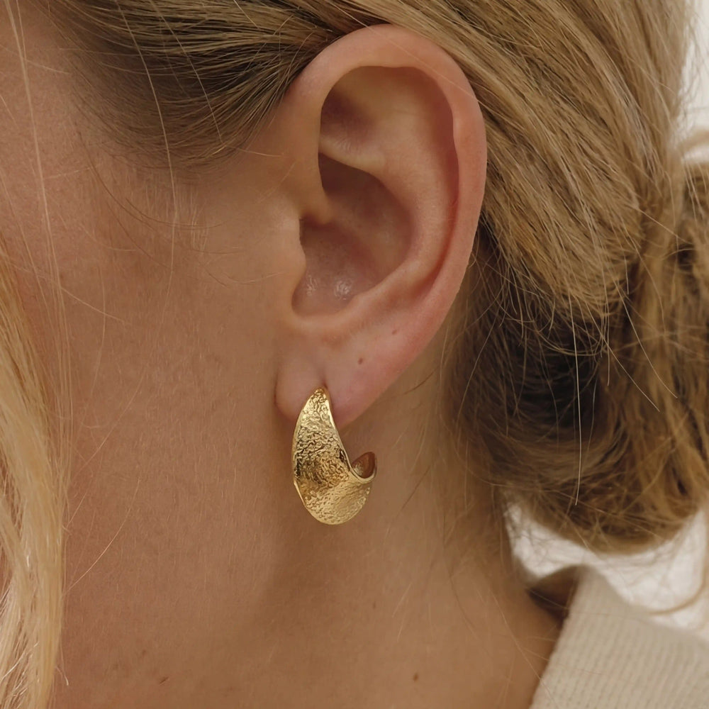 Close up of textured gold chunky hoop earrings on ear, hypoallergenic stainless steel jewelry for sensitive ears, waterproof everyday earrings for women.