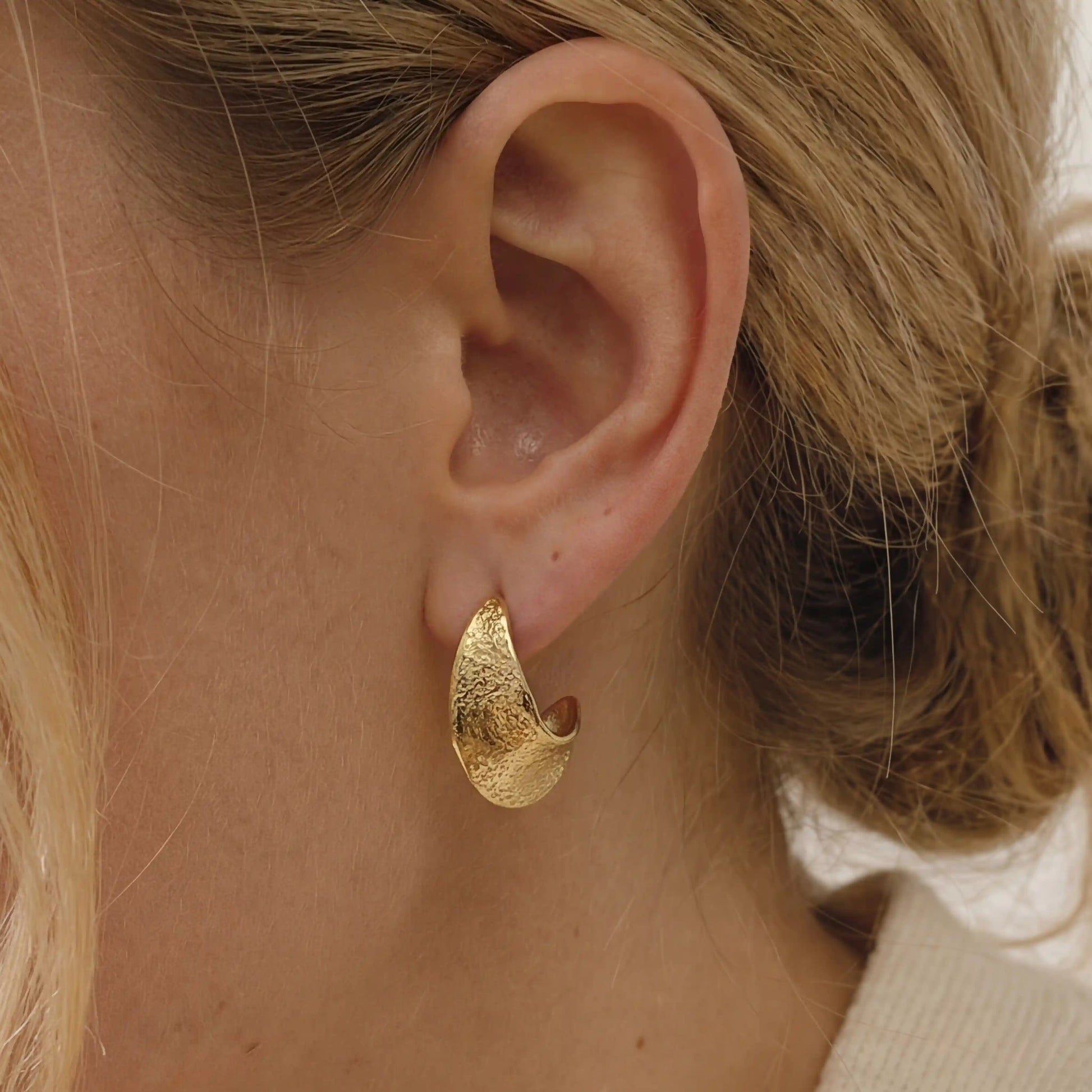 Close up of textured gold chunky hoop earrings on ear, hypoallergenic stainless steel jewelry for sensitive ears, waterproof everyday earrings for women.