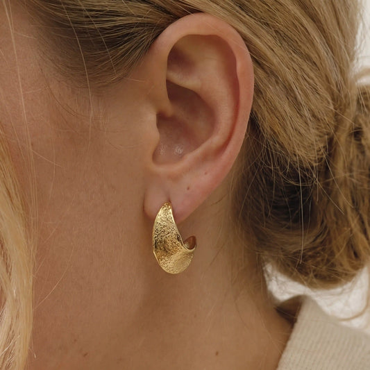 Close up of textured gold chunky hoop earrings on ear, hypoallergenic stainless steel jewelry for sensitive ears, waterproof everyday earrings for women.