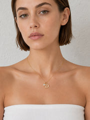 Close-up of a gold initial necklace with clear zircon charm at the collarbone