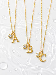 Detail view of the gold letter pendant and round zircon charm on a fine chain