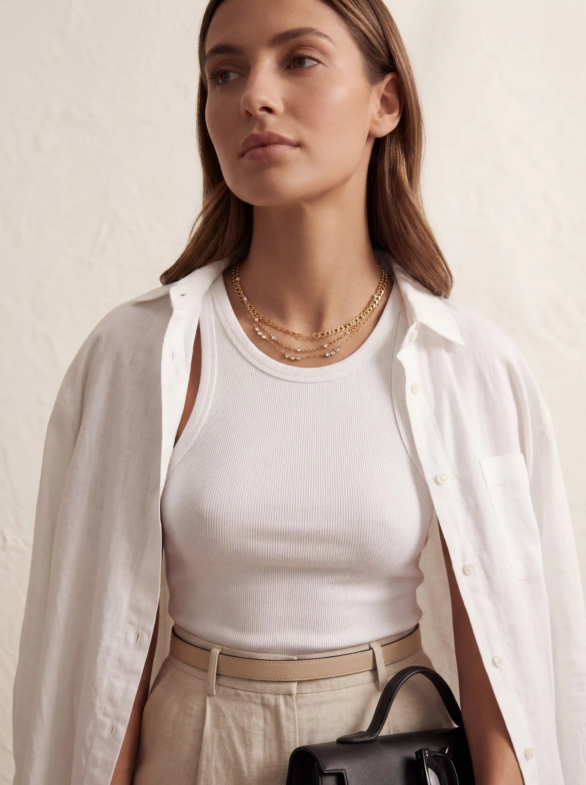 Lifestyle photography of woman wearing curated gold necklace stack with casual white button down shirt.