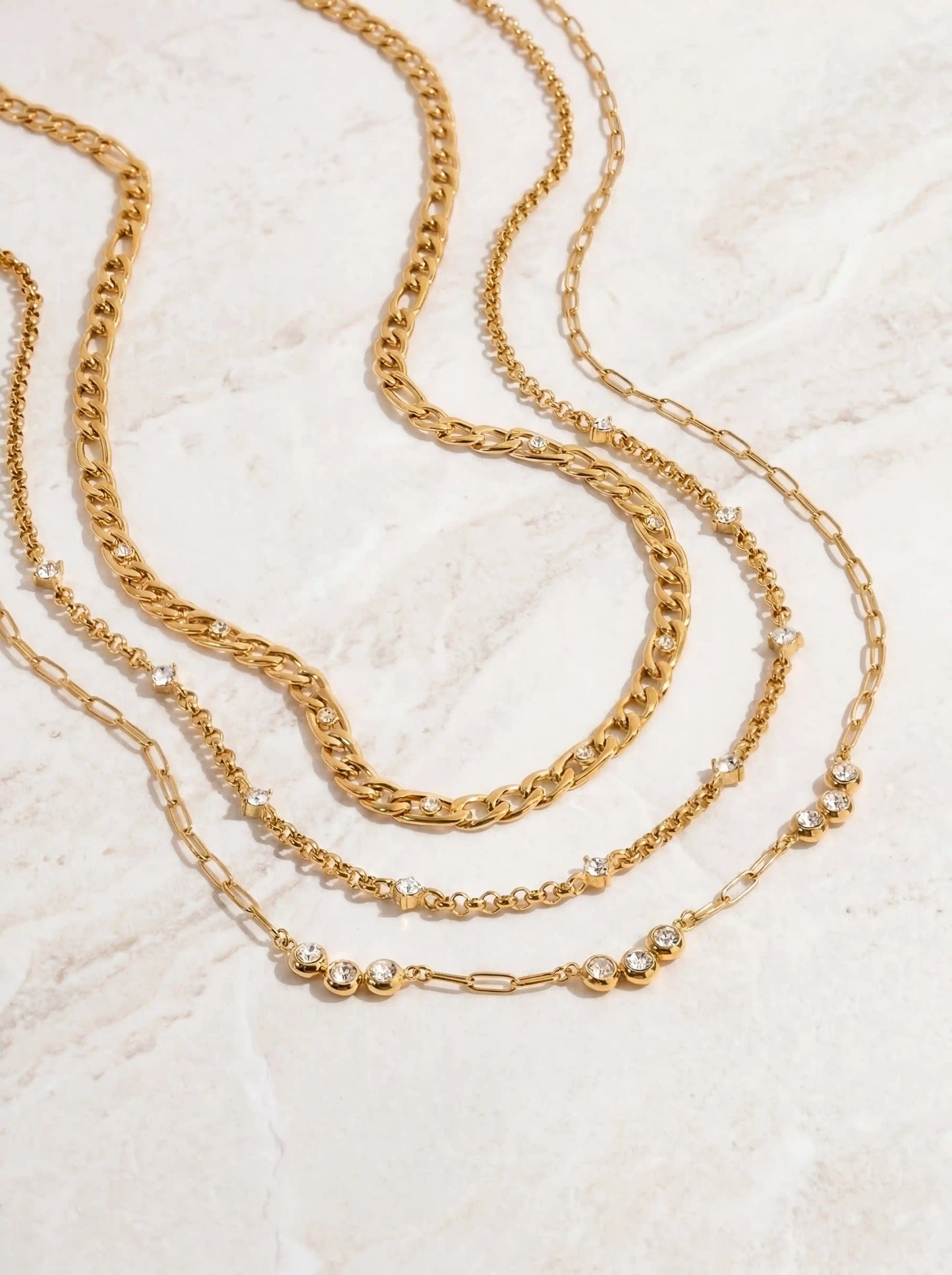 Aesthetic product photography of three layer gold necklace set gracefully draped on white marble.