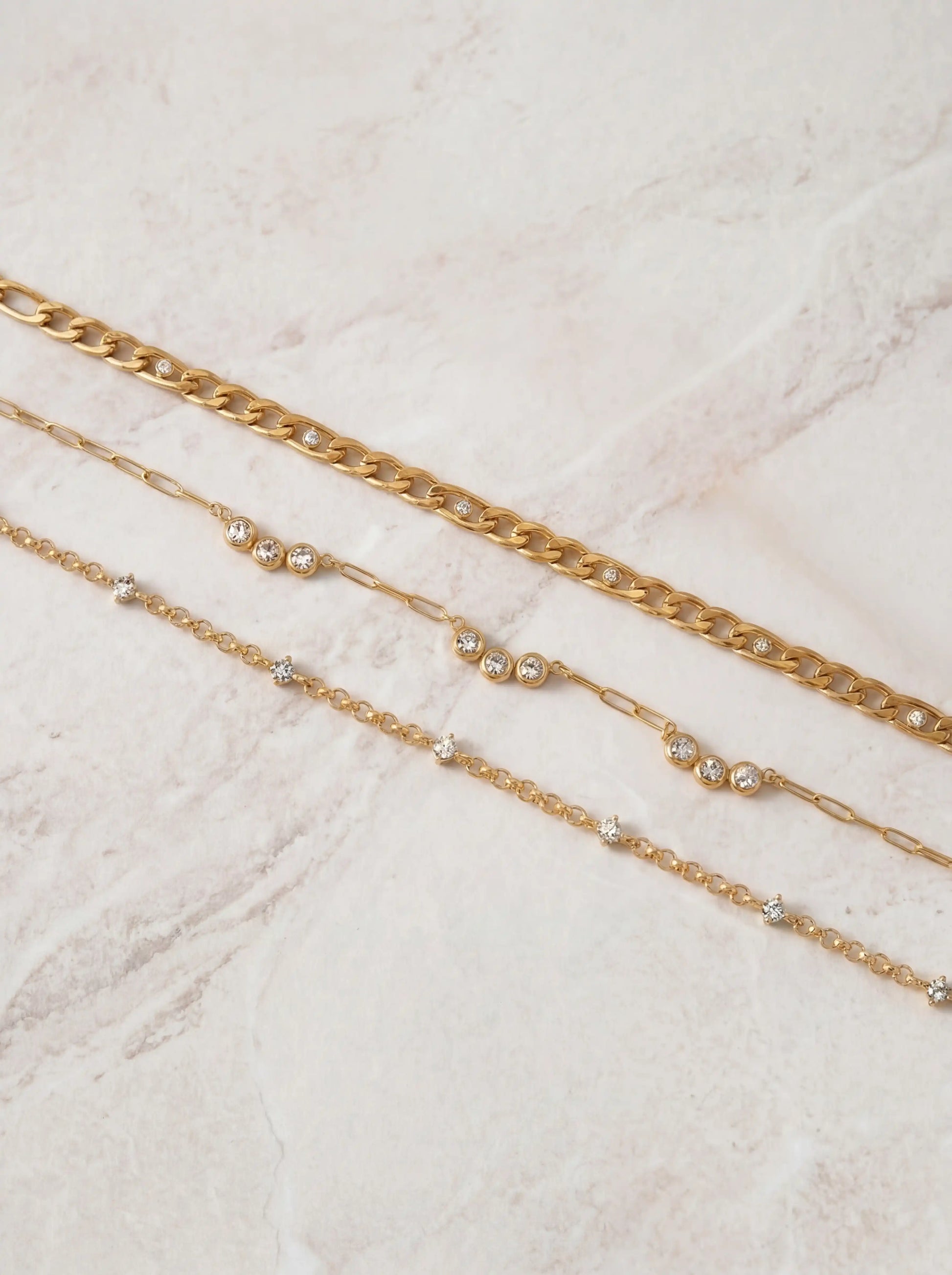 Minimalist flat lay of three gold layering necklaces showing chain textures and crystal details.