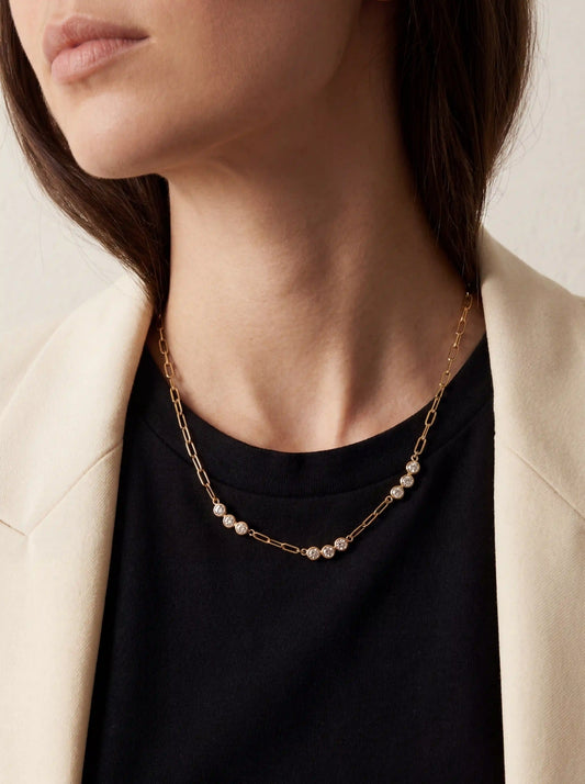 Close up of woman wearing gold Trinity crystal paperclip necklace with black top and white blazer.