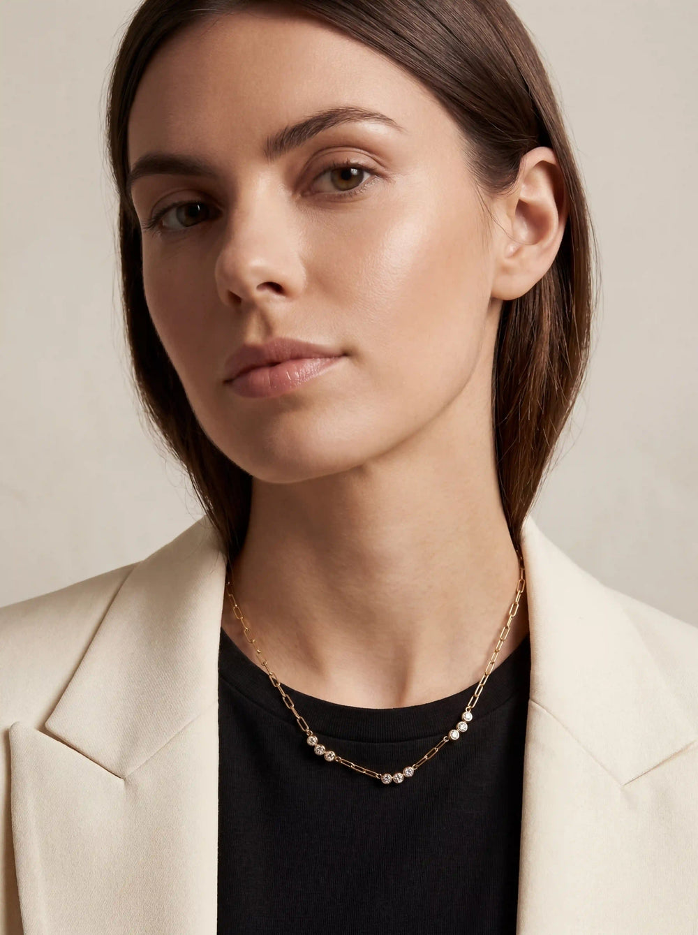 Lifestyle photography of brunette woman styling delicate gold paperclip crystal necklace everyday essential.