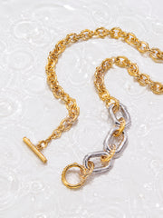 Two-tone chunky chain necklace with gold and silver links on a white water ripple background