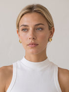 Two-tone sculptural stud earrings worn with mixed-metal jewelry in a neutral outfit