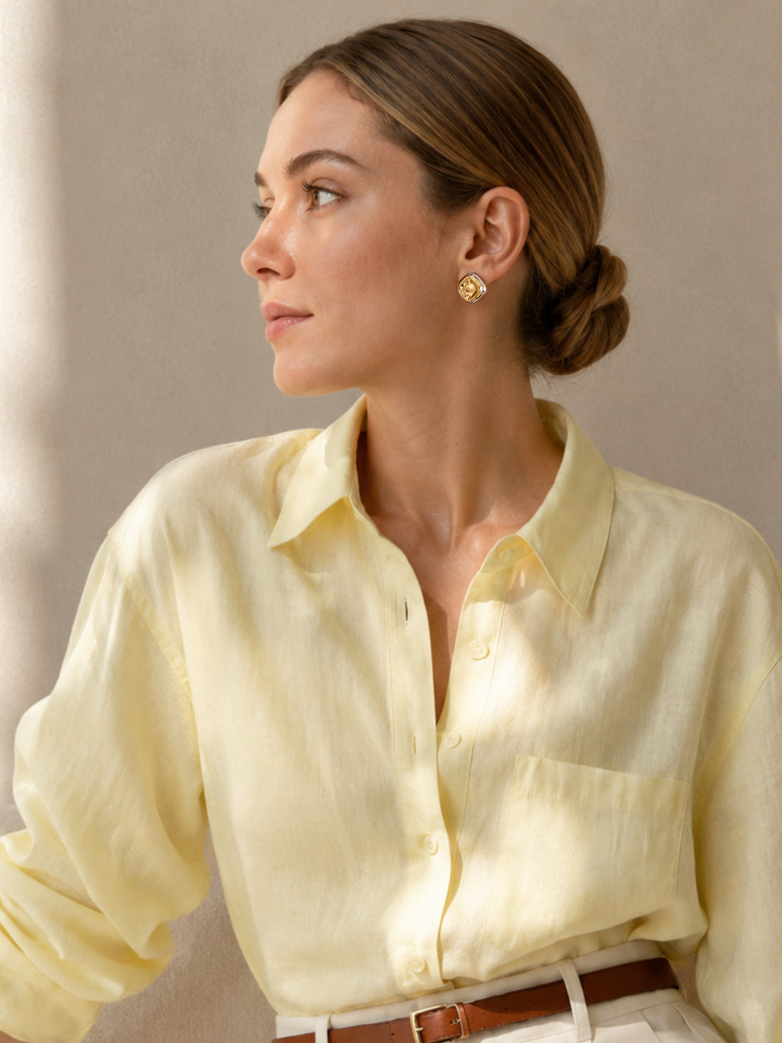 Gold and silver sculptural stud earrings worn with pale yellow shirt