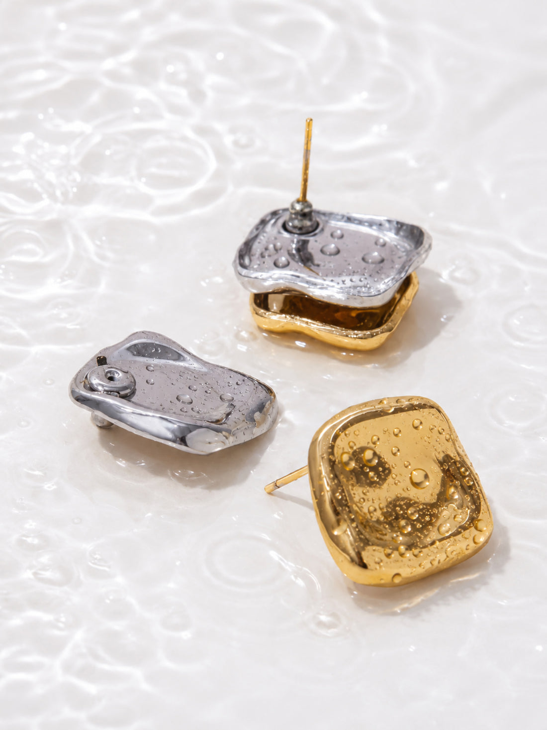 Two-tone sculptural stud earrings showing gold front and silver back on light background