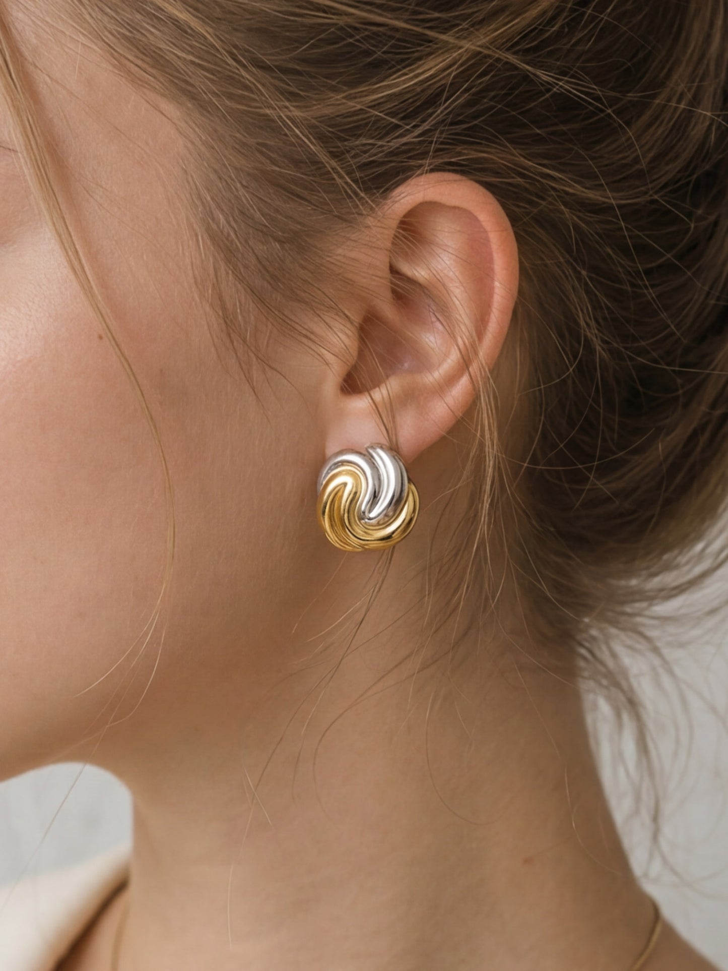 Two-tone swirl stud earrings worn by model in close-up ear shot