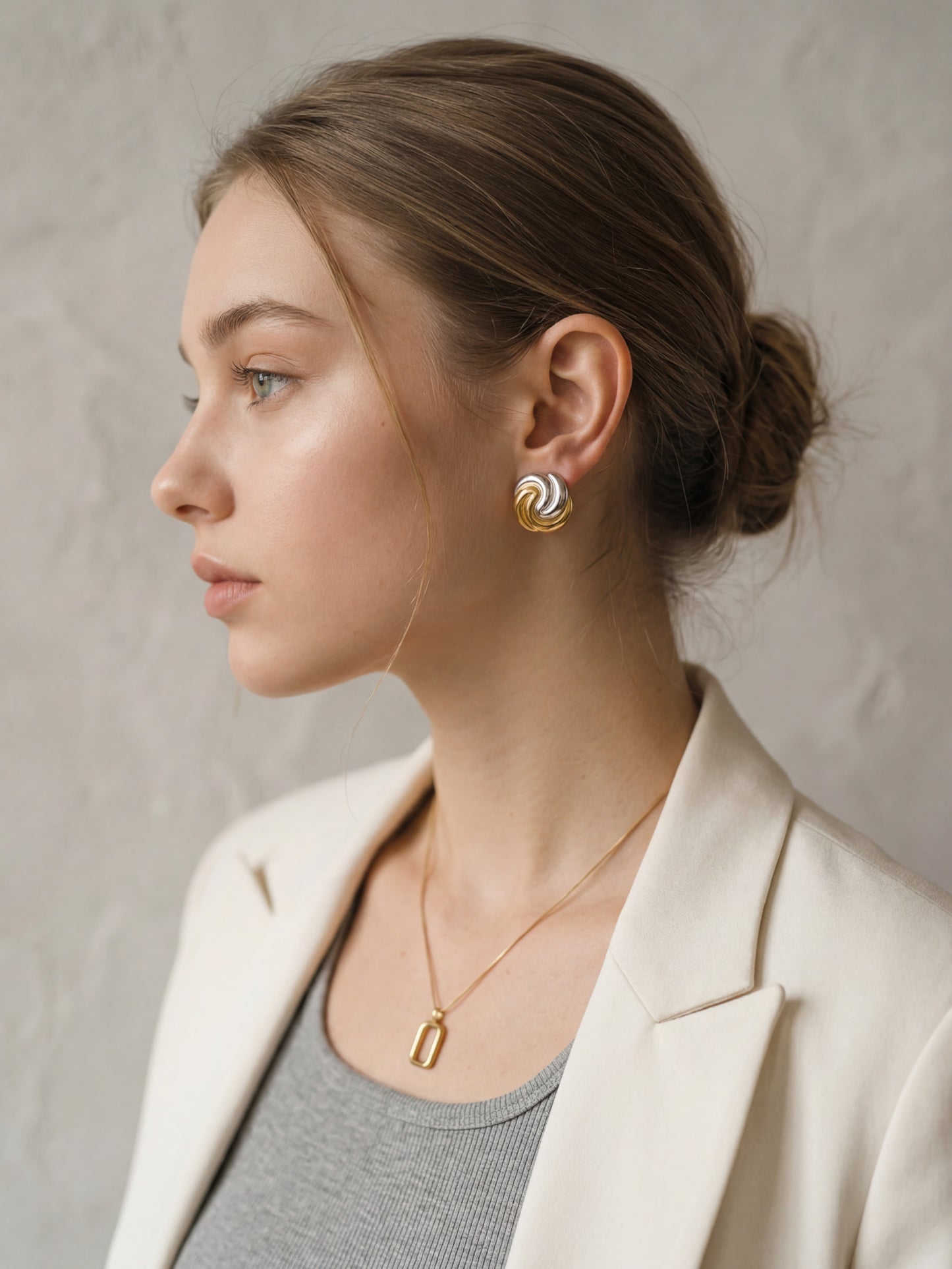 Model wearing mixed metal swirl earrings with beige blazer