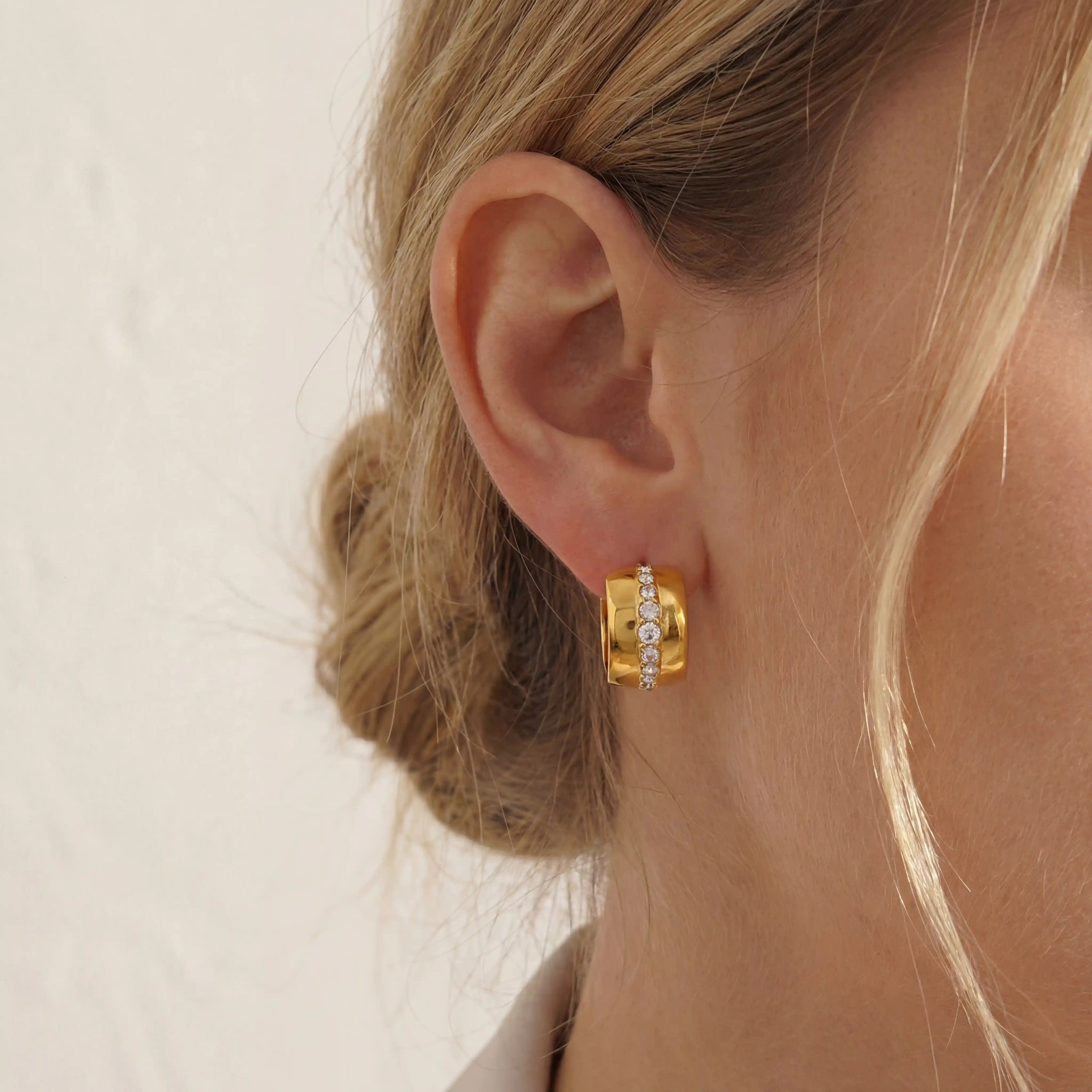 Close up of woman wearing gold Vega chunky hoop earrings with vertical crystal stripe detail.