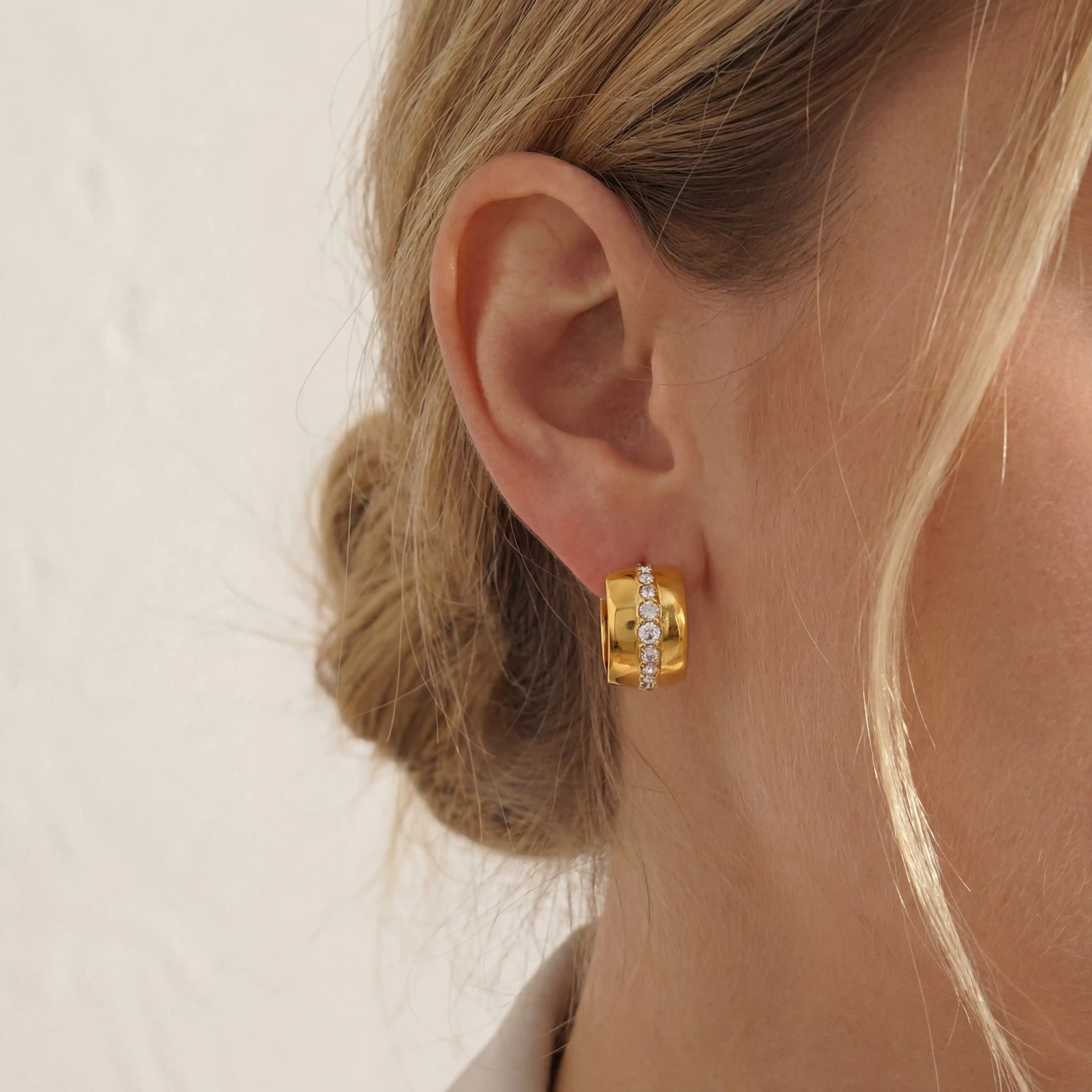 Close up of woman wearing gold Vega chunky hoop earrings with vertical crystal stripe detail. Main image