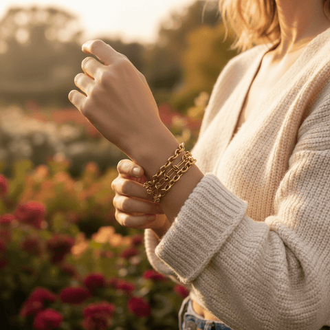 Lifestyle image of a woman in a cozy white sweater wearing The Amalfi Layering Set in a sunlit flower garden, showing the jewelry's effortless, everyday elegance.