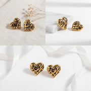 Aesthetic product photography of gold and black leopard heart studs on white background.