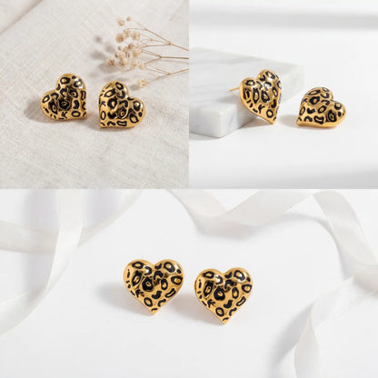 Aesthetic product photography of gold and black leopard heart studs on white background.