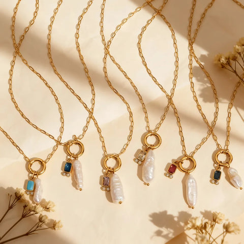 A beautiful flat lay of several Astoria Necklaces by Luminova, showcasing a variety of colorful birthstone charms paired with unique baroque pearls on gold chains.