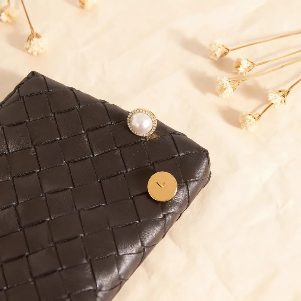 The Athena Studs styled next to a classic woven leather wallet, illustrating them as a timeless, 'quiet luxury' accessory for the sophisticated woman.