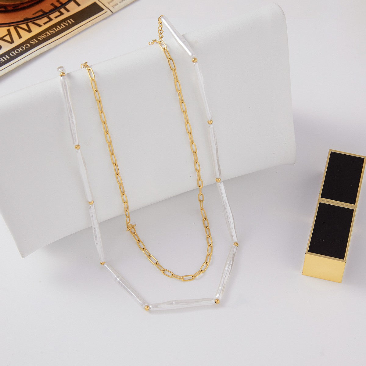 An artistic flat lay of The Callisto Necklace styled with a modern lipstick case, illustrating it as an essential accessory for a chic, modern woman.