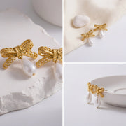 Aesthetic product details of textured gold bow earrings with pearl on white stone background.