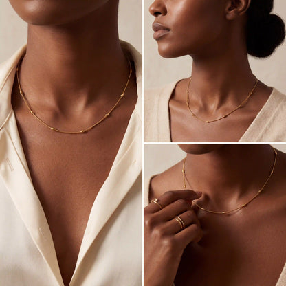 Model with dark skin styling minimalist gold beaded chain necklace layering essential.