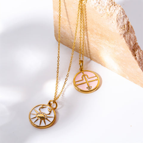 Pink and white enamel zodiac pendants Cancer and Libra gold coin necklace on stone.
