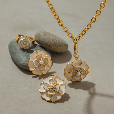 A close-up of the complete Fleur Collection, focusing on the beautiful craftsmanship of the white enamel and gold on the necklace, earrings, and ring.
