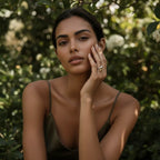 Model in a garden setting, her hand resting on a green bush to display the artistic, two-tone design of the Fluid Pebble Ring in natural light.