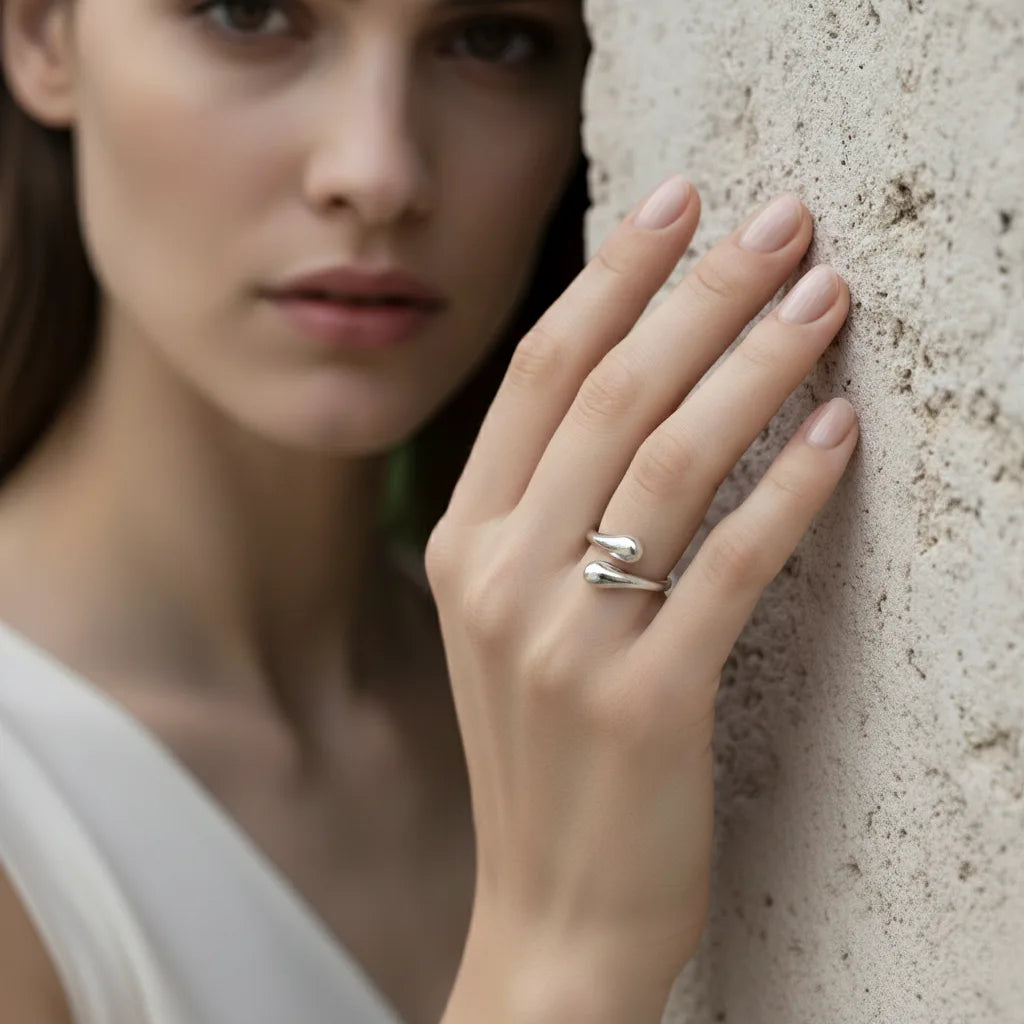 An elegant model wearing the all-silver Fluid Pebble Ring, her hand resting against a stone wall, emphasizing the ring's cool, modern vibe.
