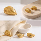 Aesthetic flat lay of gold shell earrings on beige stone and linen background.