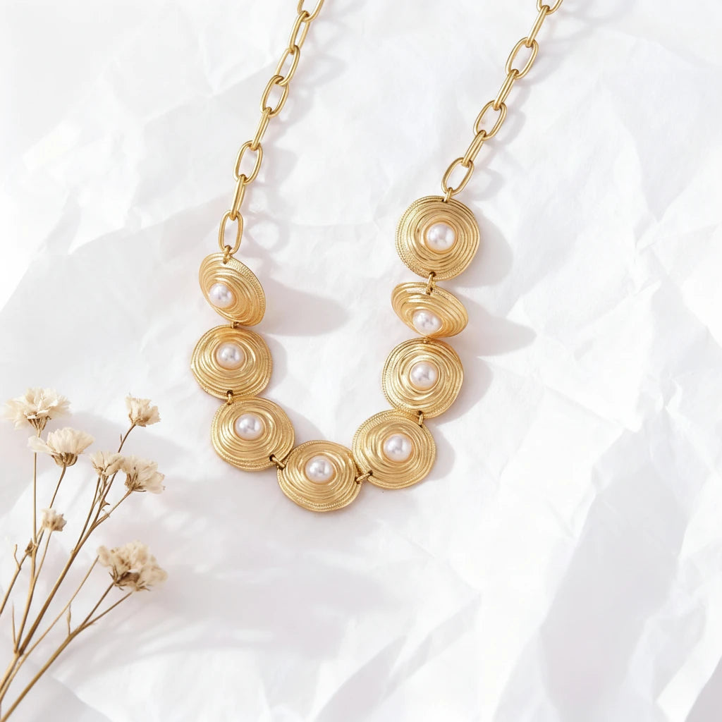 The Hera Necklace displayed on luxurious, rumpled white silk, showing the brilliant contrast between the polished pearls and the textured gold medallions